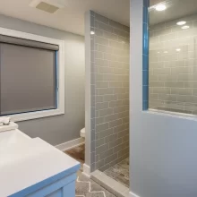 Bathroom with white vanity, framed mirror, gray subway tile shower, and wood-look flooring