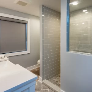 Bathroom with white vanity, framed mirror, gray subway tile shower, and wood-look flooring