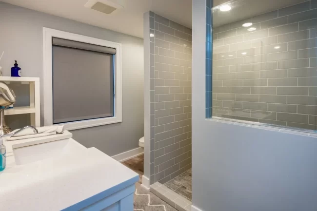 Bathroom Vanity with Gray Tile Shower | Pennings & Sons Bathroom with white vanity, framed mirror, gray subway tile shower, and wood-look flooring