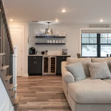 Living room view with custom staircase, black balusters, wet bar cabinetry, and lake-facing windows