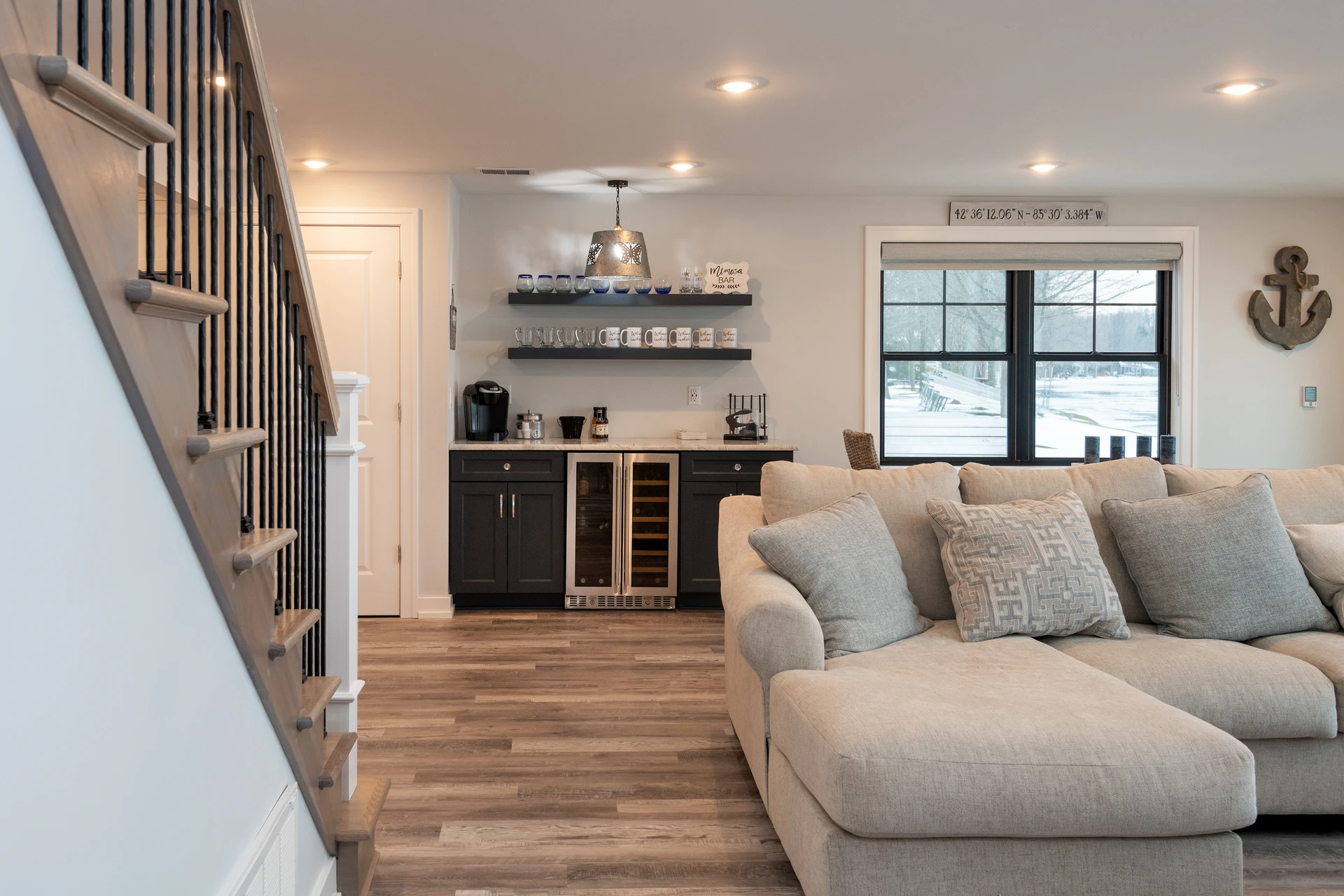 Living room view with custom staircase, black balusters, wet bar cabinetry, and lake-facing windows