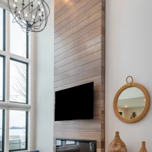 Two-story living room feature wall with horizontal wood paneling, linear fireplace, mounted TV, and tall lake-facing windows