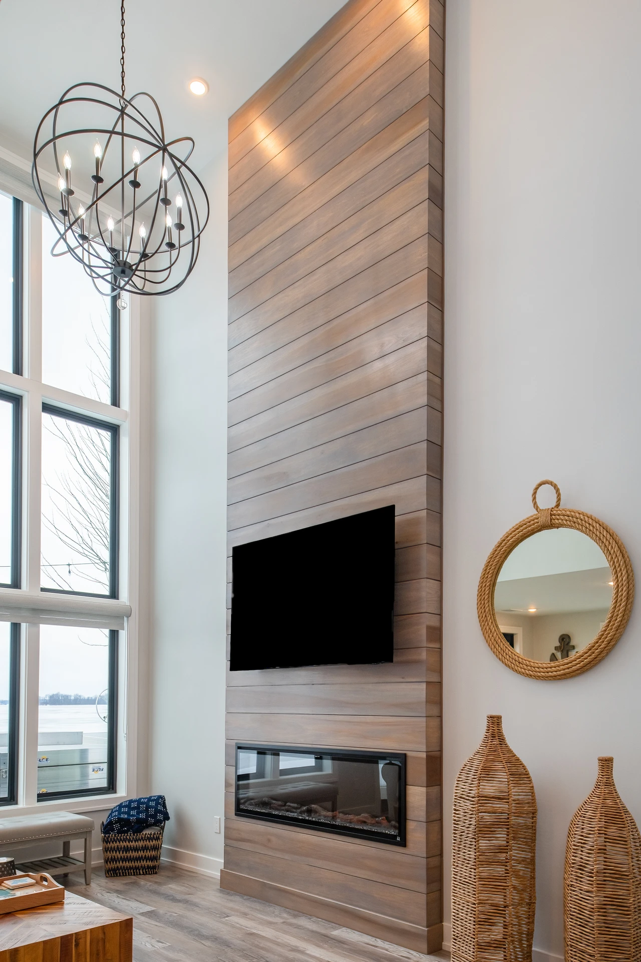Two-story living room feature wall with horizontal wood paneling, linear fireplace, mounted TV, and tall lake-facing windows
