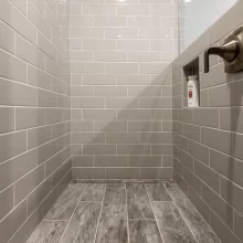 Walk-in shower with gray subway tile walls, recessed niche, wood-look tile floor, and glass partition
