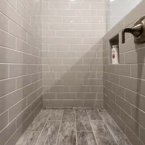 Walk-in shower with gray subway tile walls, recessed niche, wood-look tile floor, and glass partition