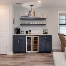 Built-in wet bar with dark cabinetry, floating shelves, wine fridge, beverage station, and lake view window