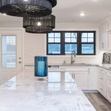 White kitchen with large marble-look island, black-framed window, subway tile backsplash, and pendant lighting