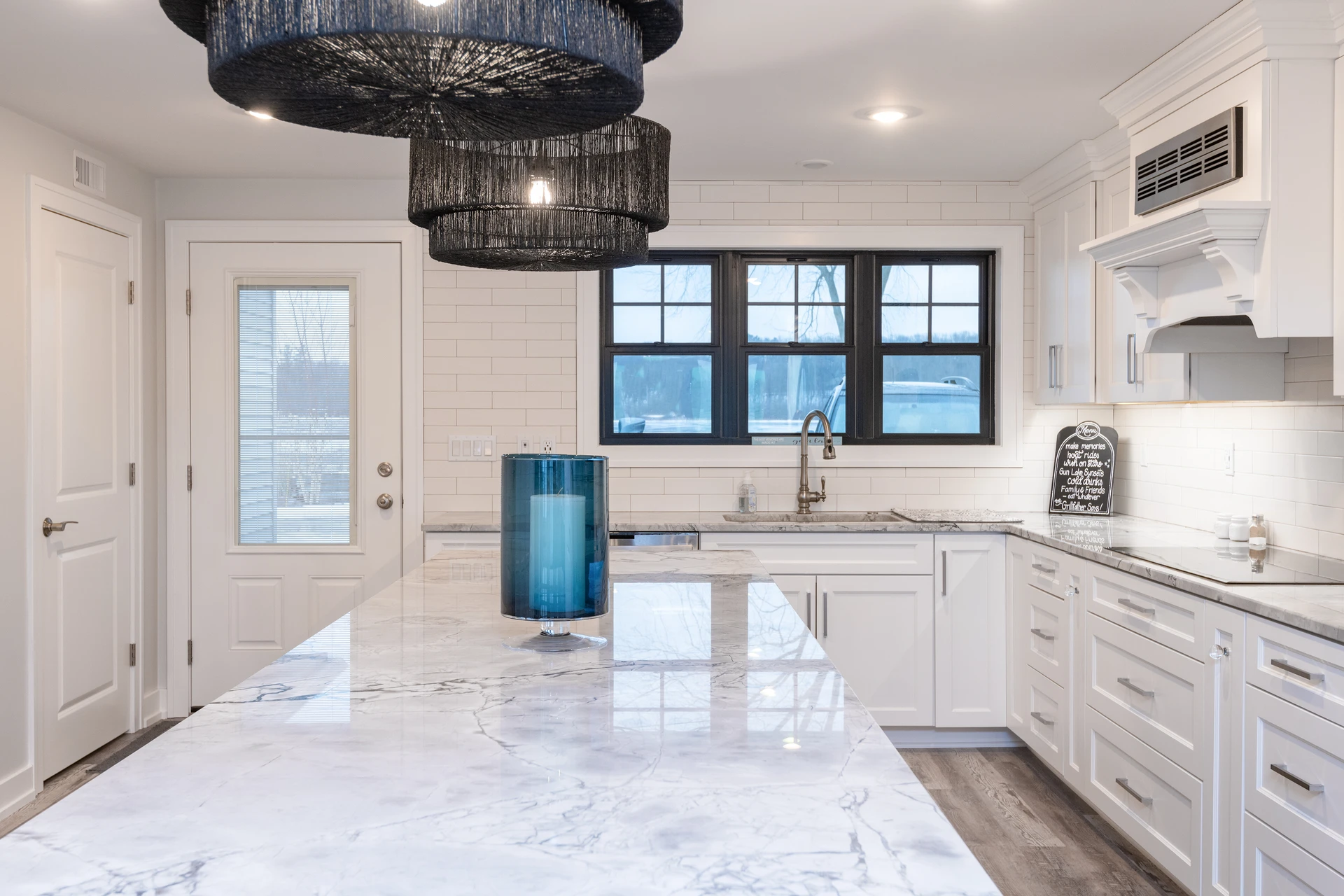White kitchen with large marble-look island, black-framed window, subway tile backsplash, and pendant lighting