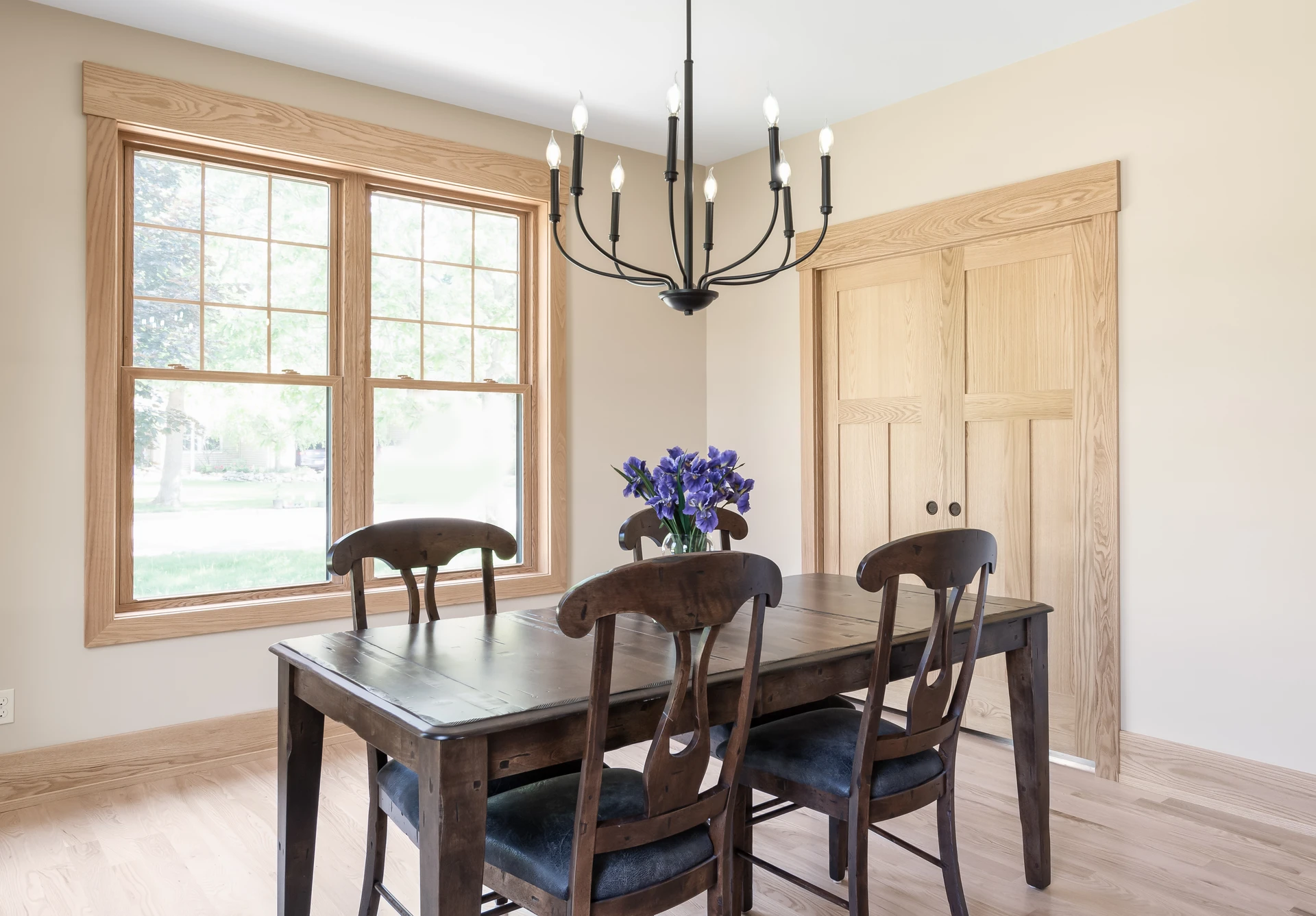 Dining room with natural wood window trim, matching closet doors, light wood flooring, and black chandelier