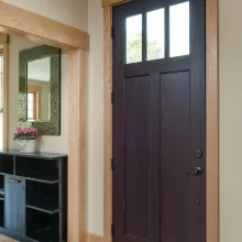 Dark entry door with natural wood casing, matching base trim, and nearby built-in entry storage
