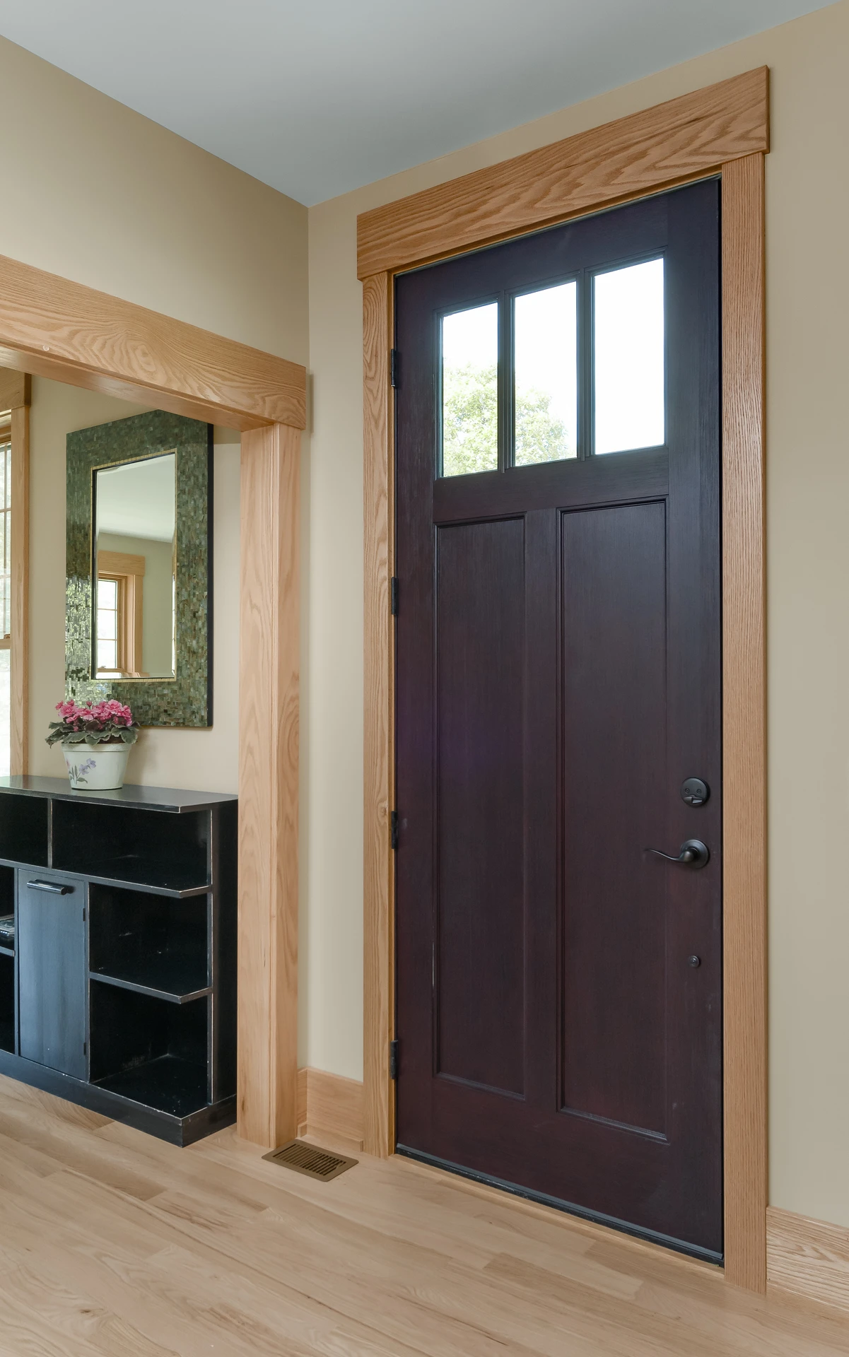 Dark entry door with natural wood casing, matching base trim, and nearby built-in entry storage