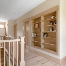 Upstairs hallway with custom built-in wood bookshelves, natural wood trim, matching doors, and stair railing