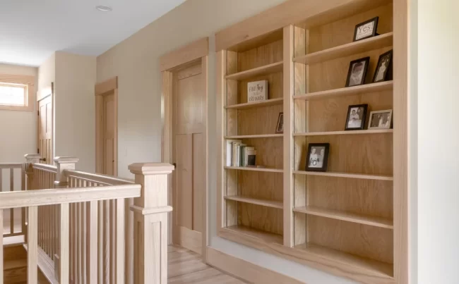 Kalamazoo - New Home Upstairs hallway with custom built-in wood bookshelves, natural wood trim, matching doors, and stair railing