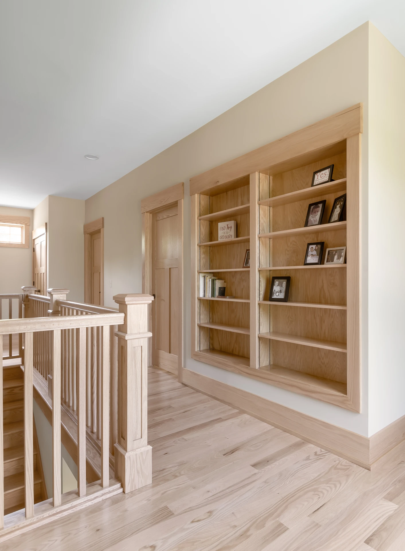 Upstairs hallway with custom built-in wood bookshelves, natural wood trim, matching doors, and stair railing