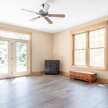 Bright living room with French doors, large window, natural wood trim, gray flooring, and ceiling fan
