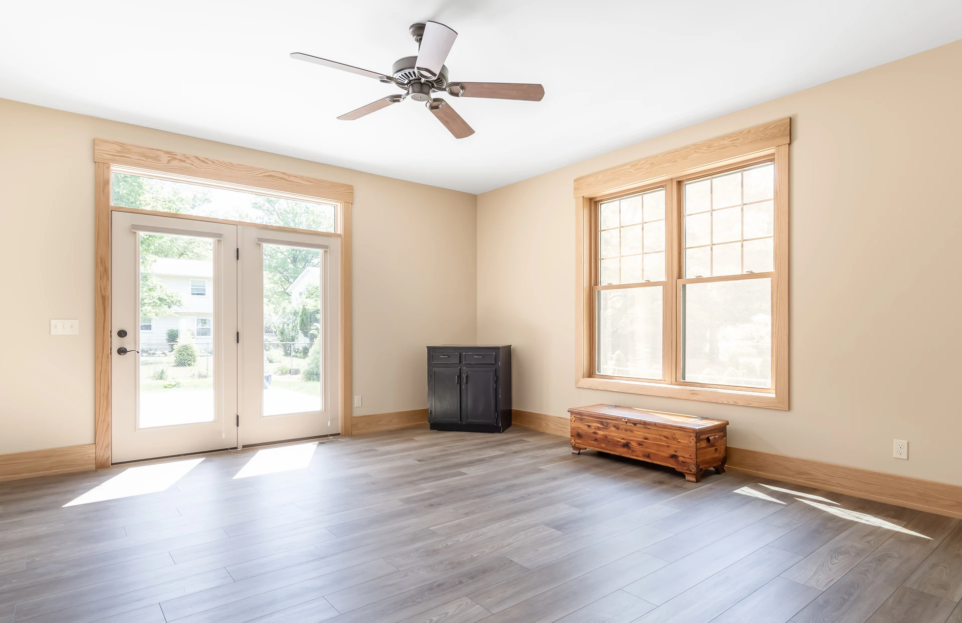 Bright living room with French doors, large window, natural wood trim, gray flooring, and ceiling fan