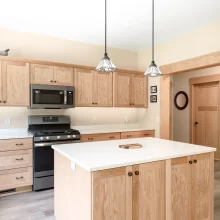 Natural wood kitchen cabinetry with a white island countertop, pendant lights, and matching wood trim