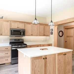 Natural wood kitchen cabinetry with a white island countertop, pendant lights, and matching wood trim
