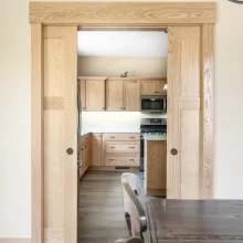Natural wood pocket doors framed with wide casing opening from the dining room into the remodeled kitchen