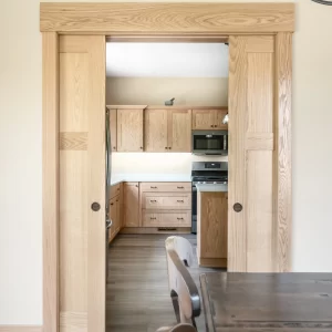 Natural wood pocket doors framed with wide casing opening from the dining room into the remodeled kitchen