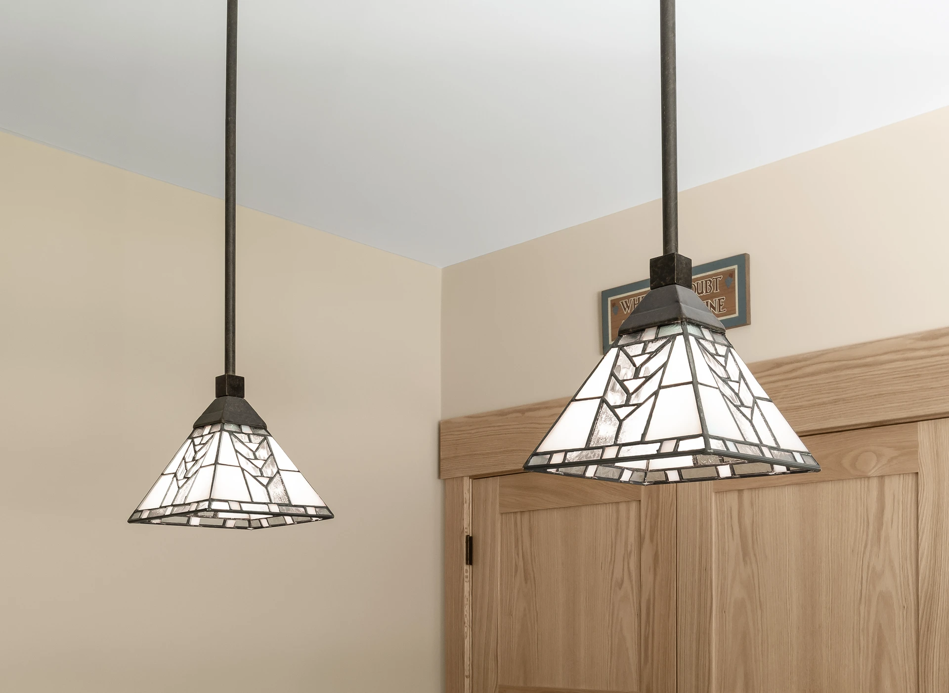Close-up of stained glass pendant lights above natural wood cabinetry and trim