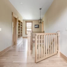Upper hallway with natural wood railing, built-in shelving, light wood flooring, and matching trim details