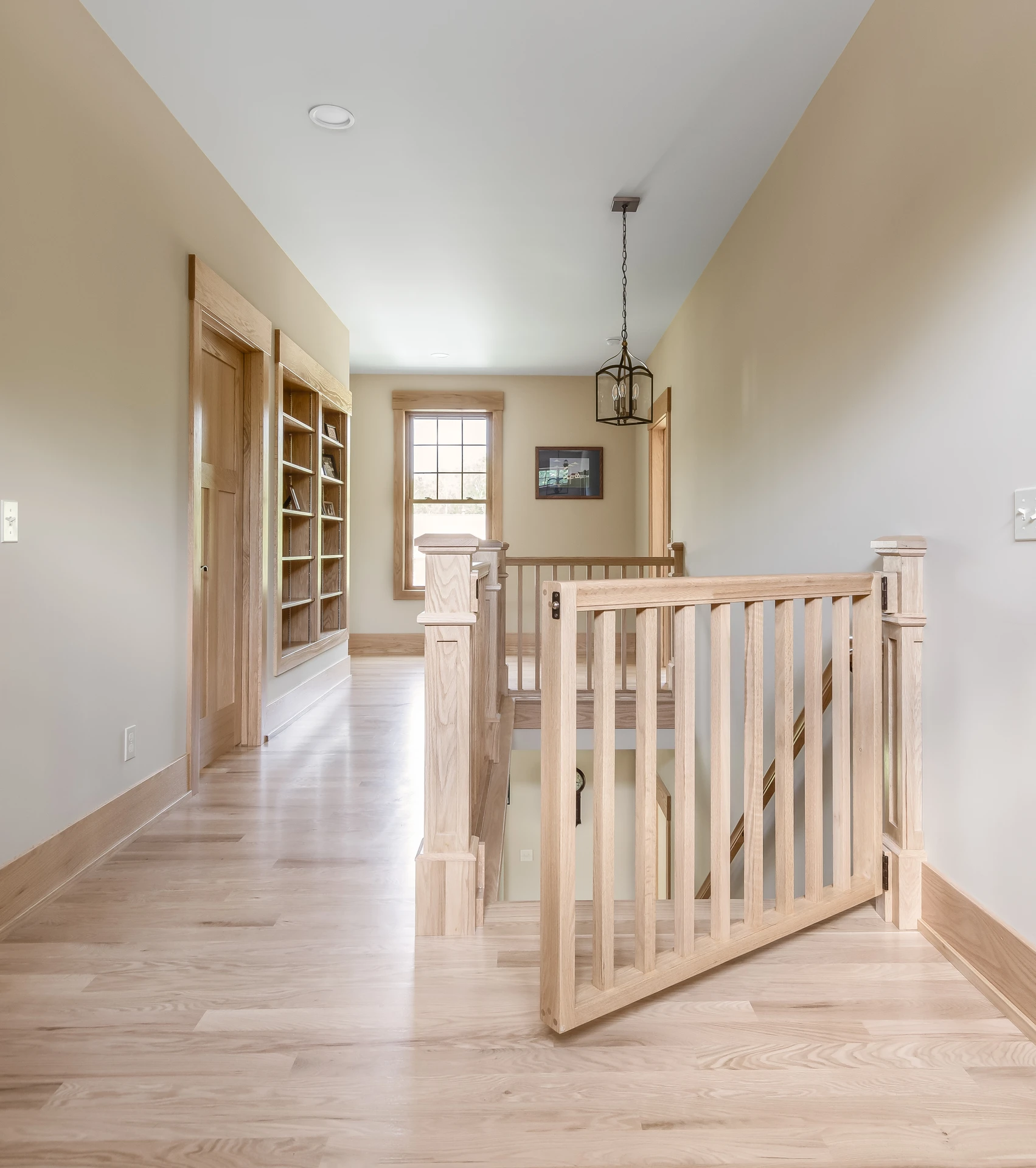 Upper hallway with natural wood railing, built-in shelving, light wood flooring, and matching trim details