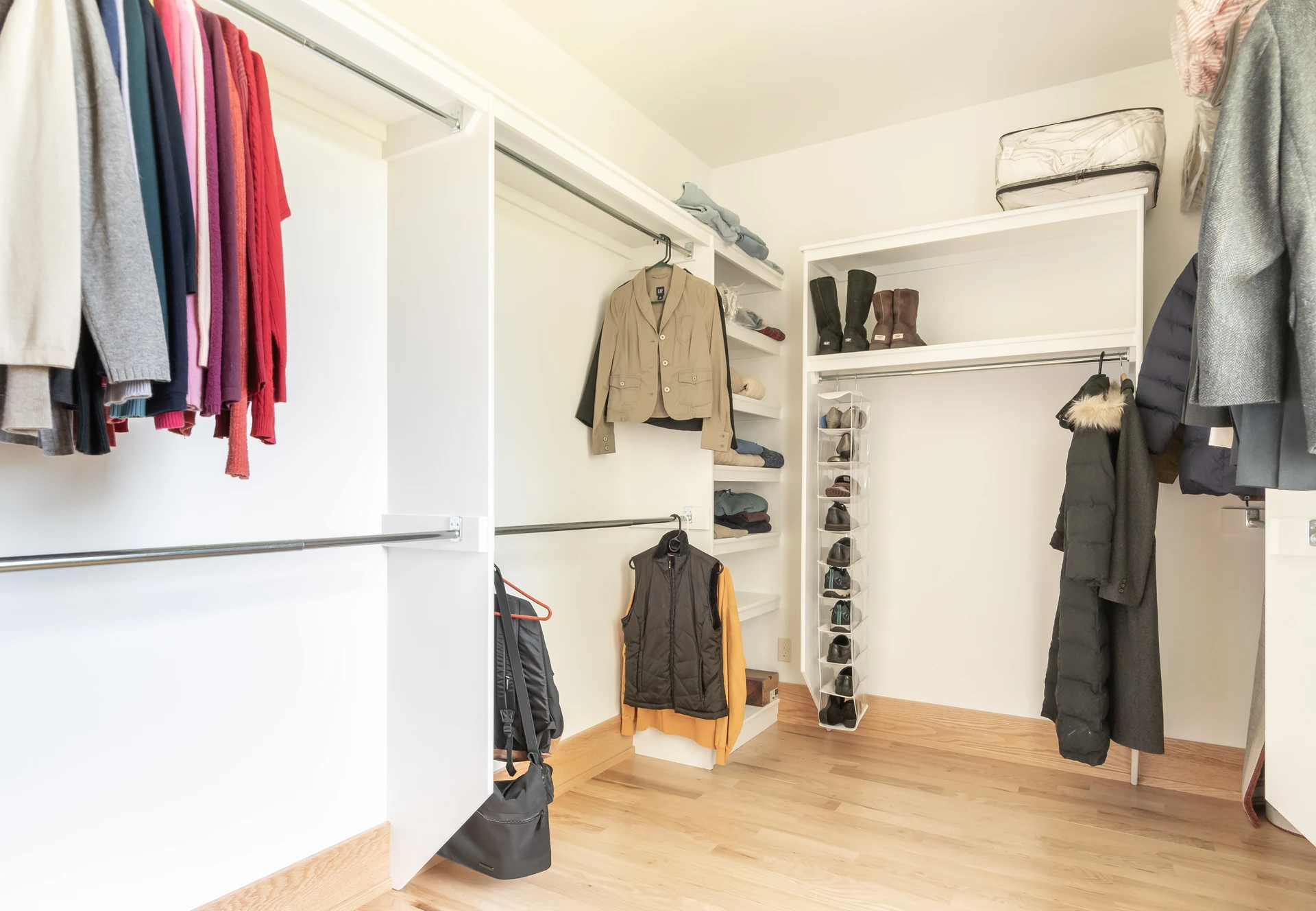 Walk-in closet with open shelving, hanging rods, light wood flooring, and organized clothing storage