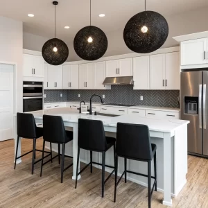 White kitchen with quartz island, black bar stools, black globe pendant lights, stainless appliances, and gray herringbone tile backsplash