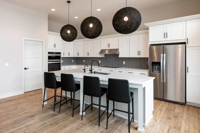 White Kitchen with Black Globe Pendant Lights | Pennings & Sons White kitchen with quartz island, black bar stools, black globe pendant lights, stainless appliances, and gray herringbone tile backsplash