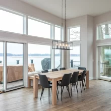 Dining room with wood table, black chairs, modern rectangular chandelier, tall windows, sliding glass doors, and lake views