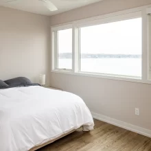 Guest Bedroom with white bedding, wood-look flooring, ceiling fan, and large windows overlooking the lake