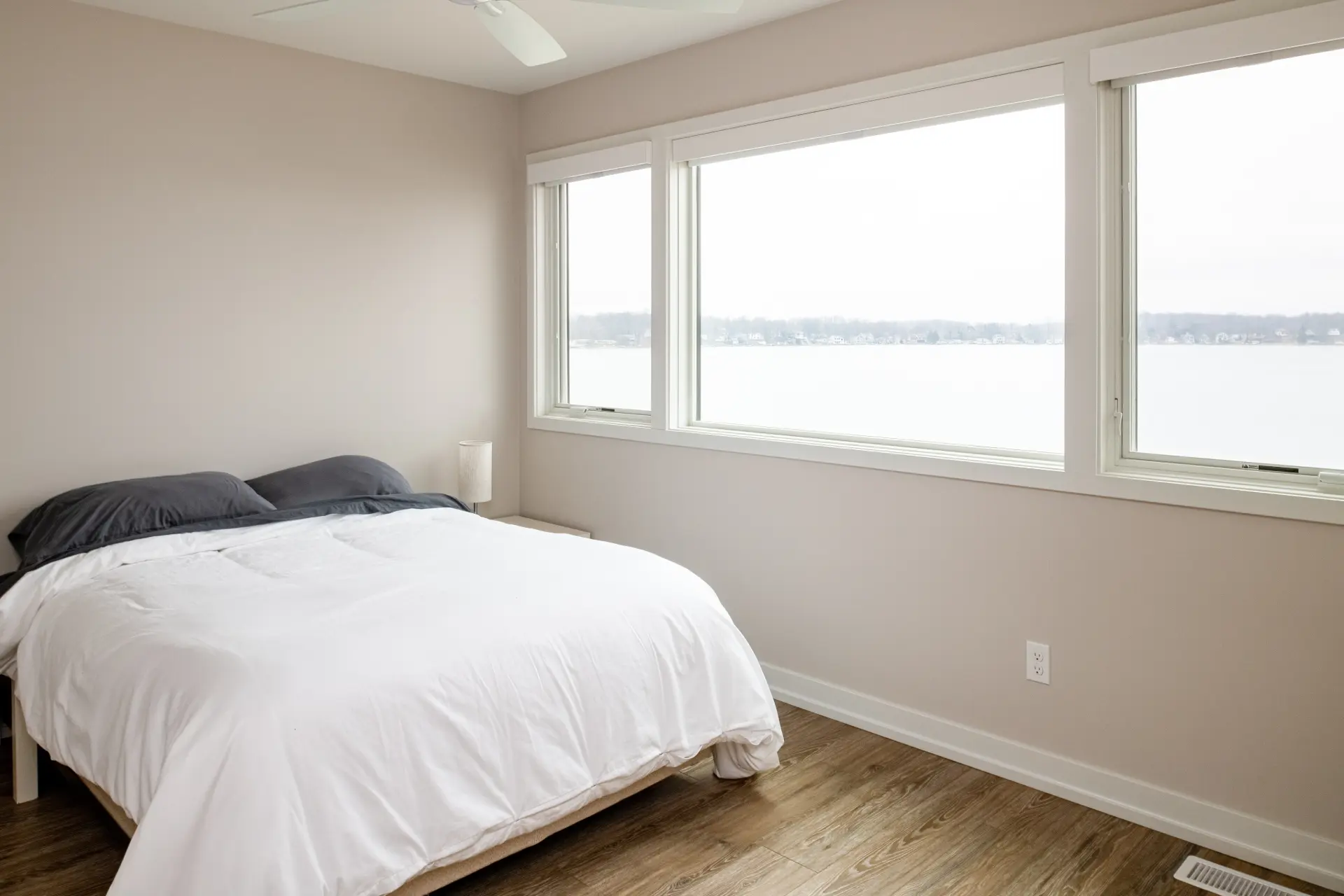Guest Bedroom with white bedding, wood-look flooring, ceiling fan, and large windows overlooking the lake