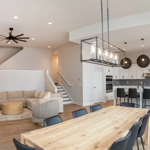 Open concept interior with dining table, living room seating, staircase, kitchen island, and modern pendant lights