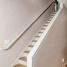 Interior staircase with wood treads, white railing, matching wall handrail, neutral walls, and wood-look flooring