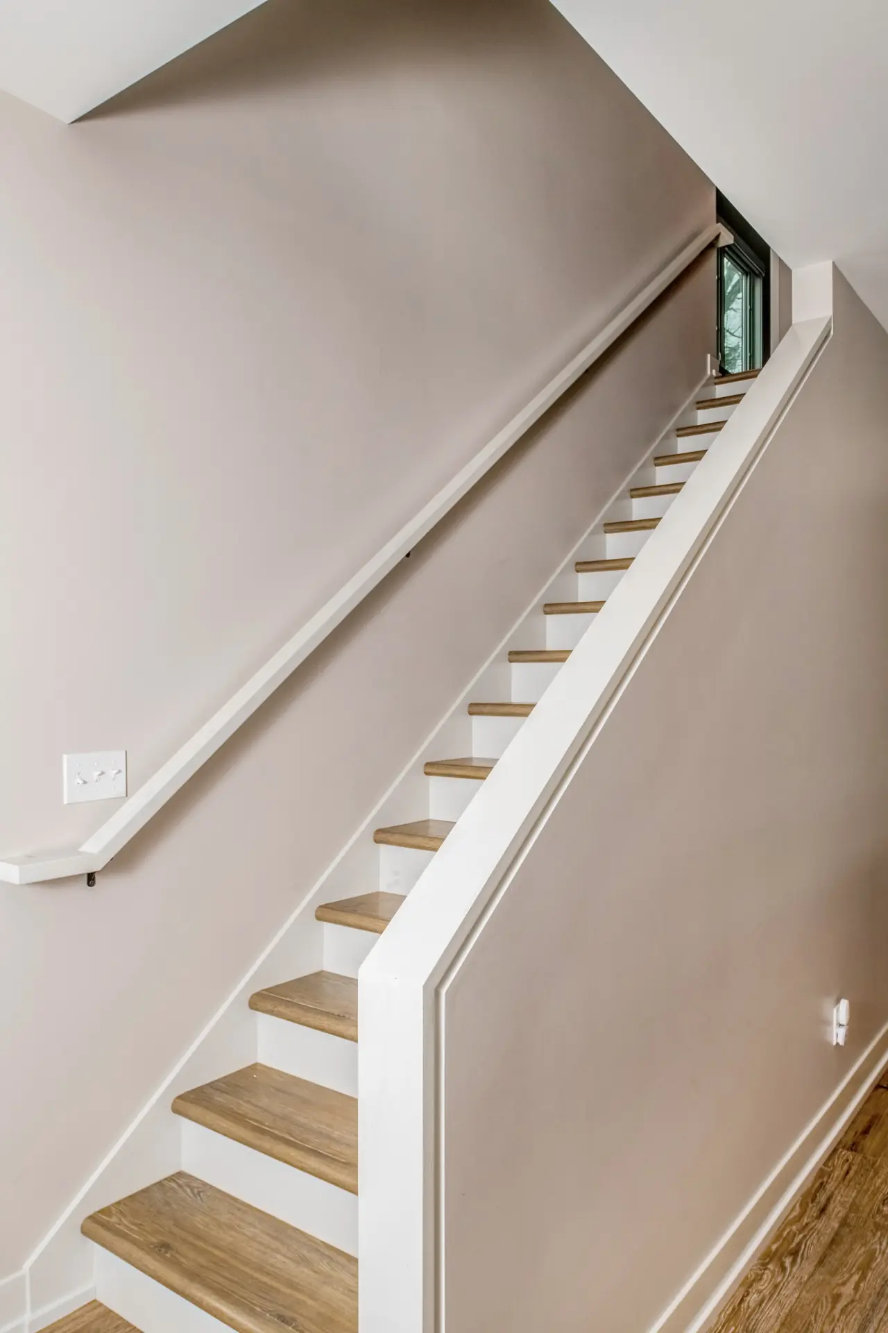 Interior staircase with wood treads, white railing, matching wall handrail, neutral walls, and wood-look flooring