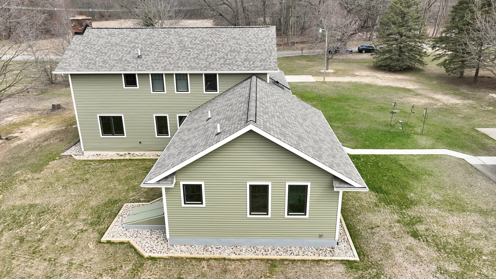 Aerial rear exterior view of green home with gray shingle roof, white trim windows, walkways, and surrounding yard
