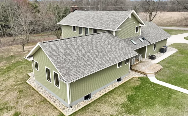 Aerial Side Exterior and Deck View | Pennings & Sons Aerial side view of green home with gray shingle roof, small deck, skylights, white trim, and landscaped perimeter