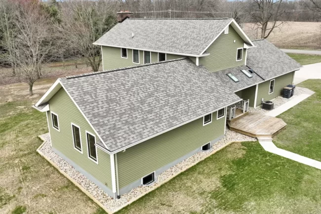 Aerial Side Exterior and Deck View | Pennings & Sons Aerial side view of green home with gray shingle roof, small deck, skylights, white trim, and landscaped perimeter