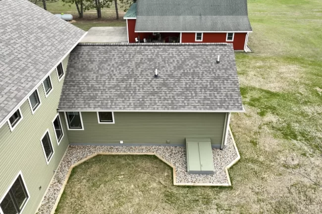 Aerial Home Roofline Exterior View | Pennings & Sons Aerial view of green home exterior with gray shingle roof, white trim windows, rock landscaping, and open lawn