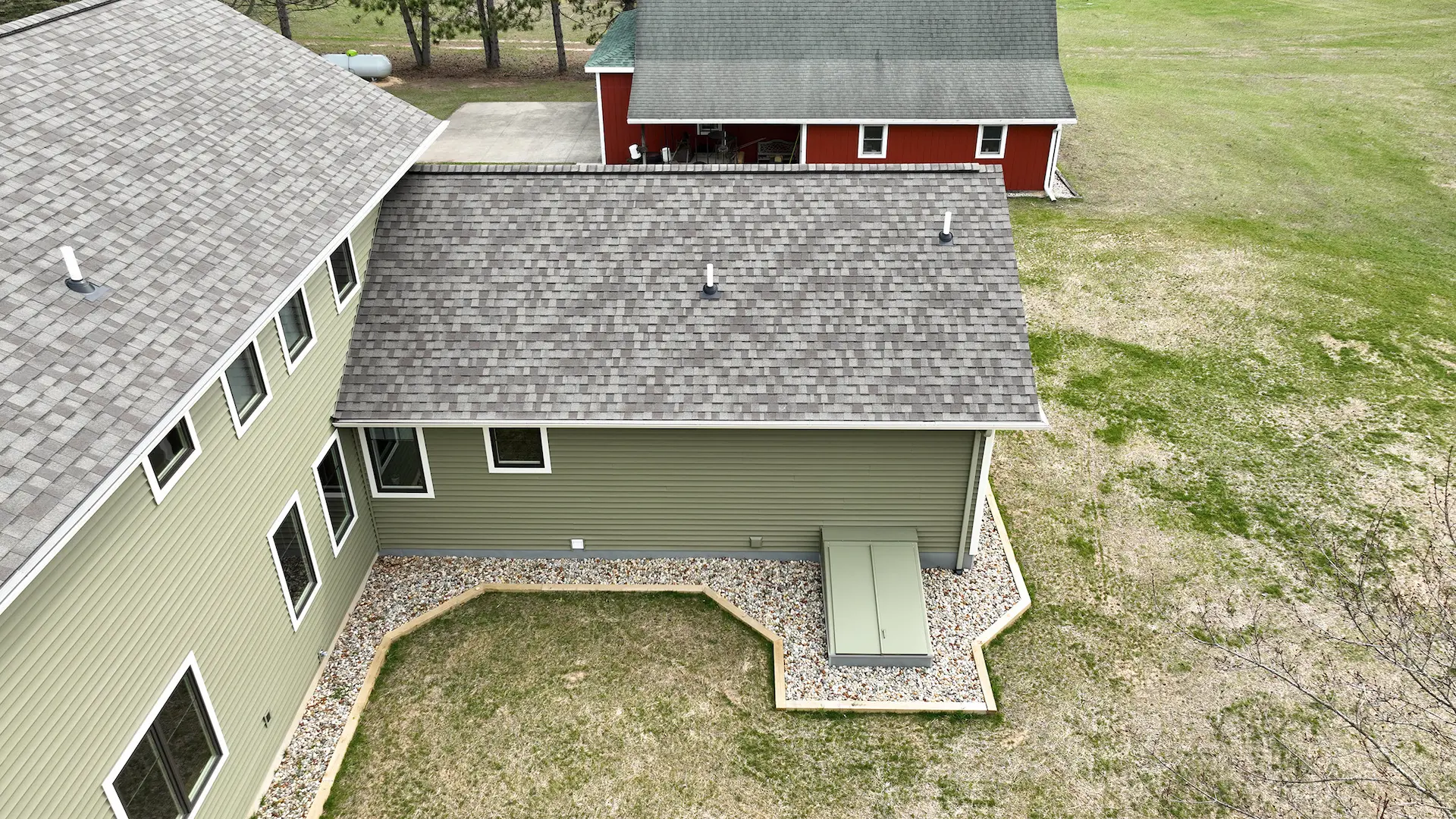 Aerial view of green home exterior with gray shingle roof, white trim windows, rock landscaping, and open lawn
