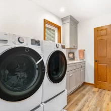 Laundry room with white front load washer and dryer, gray cabinets, wood flooring, wood door, and countertop storage