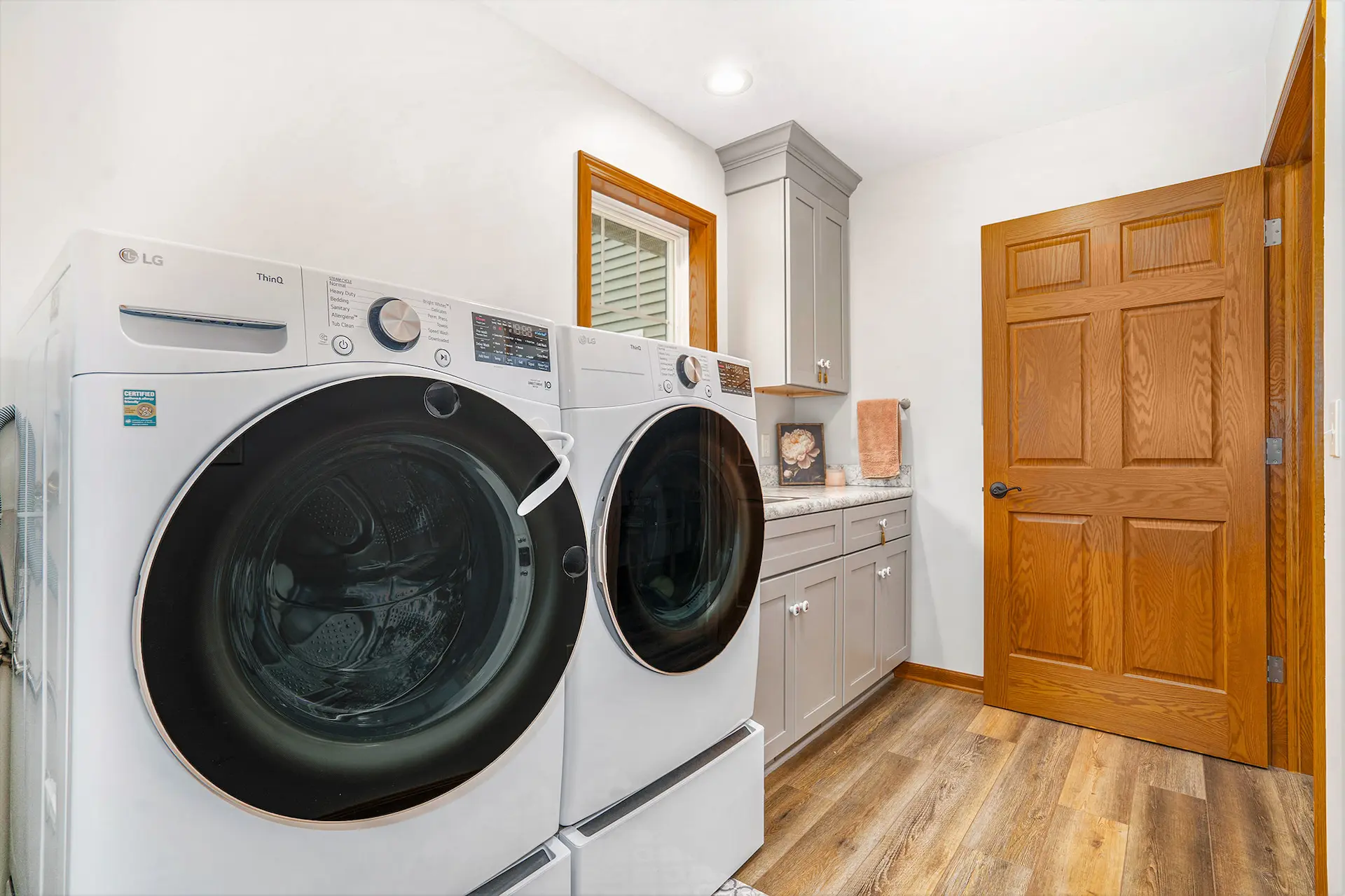 Laundry room with white front load washer and dryer, gray cabinets, wood flooring, wood door, and countertop storage