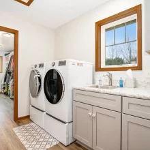 Laundry room with front load washer and dryer, gray cabinetry, utility sink, wood trim, and walk-in closet access