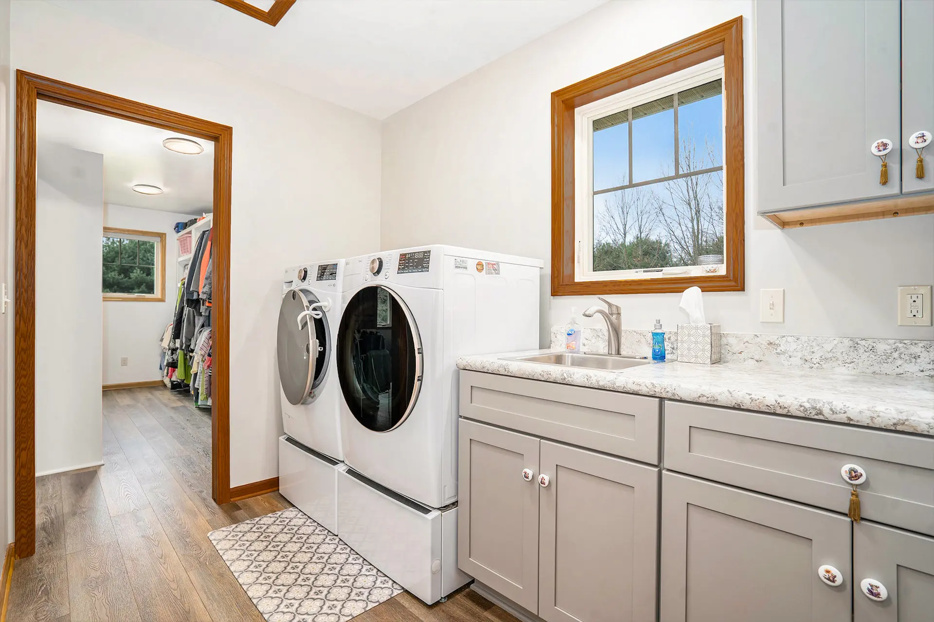 Laundry room with front load washer and dryer, gray cabinetry, utility sink, wood trim, and walk-in closet access