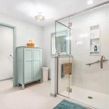 Spacious bathroom with glass shower enclosure, pale green storage cabinet, tile flooring, window, and soft blue-green trim