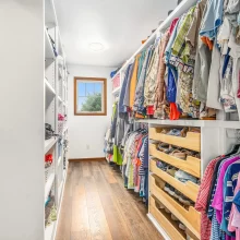 Walk-in closet with custom white shelving, hanging storage, wood flooring, shoe storage, and natural light from window