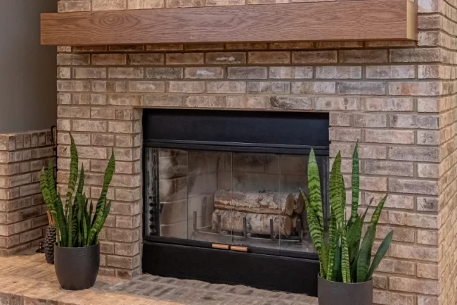 Brick Fireplace with Custom Wood Mantel | Pennings & Sons Brick fireplace with custom wood mantel, black fireplace surround, raised hearth, and indoor plants