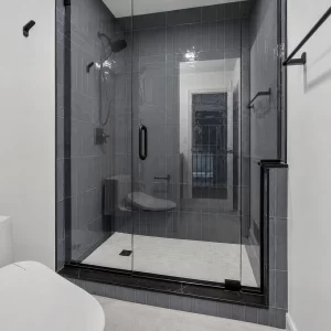 Glass shower with blue-gray wall tile, black shower hardware, handheld shower head, and light tile shower floor.