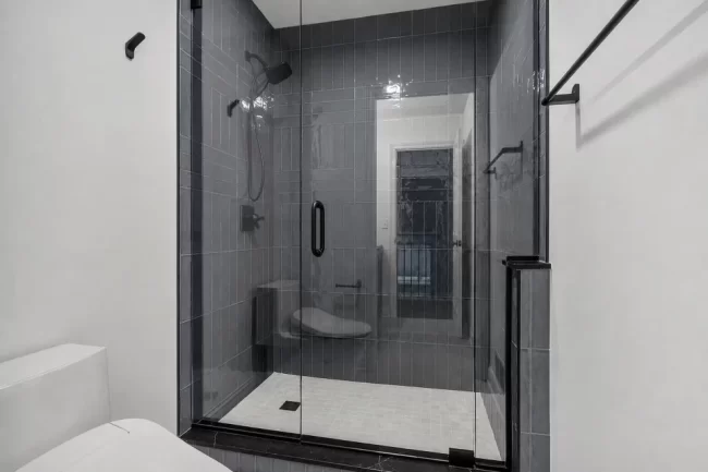 Glass Shower with Blue Gray Tile | Pennings & Sons Glass shower with blue-gray wall tile, black shower hardware, handheld shower head, and light tile shower floor.